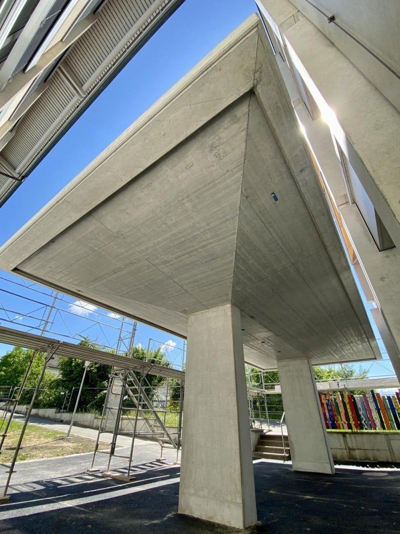 Moderne Architektur: Betonüberdachung mit blauem Himmel und Gerüsten, ergänzt durch bunte Wandkunst im Hintergrund.