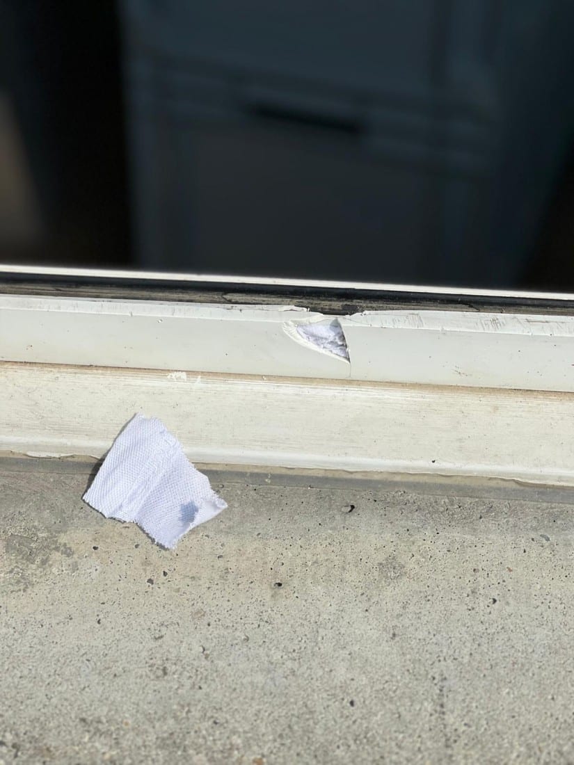 Beschädigter Fensterrahmen mit abgebrochener Stelle und Stofffetzen auf Betonuntergrund.