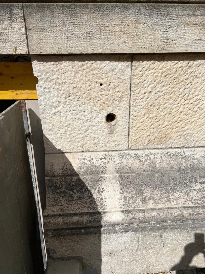 Steinmauer mit Bohrlöchern, Sonnenschatten und Baumaterialien, Textur sichtbar, Detailansicht einer Baustelle.