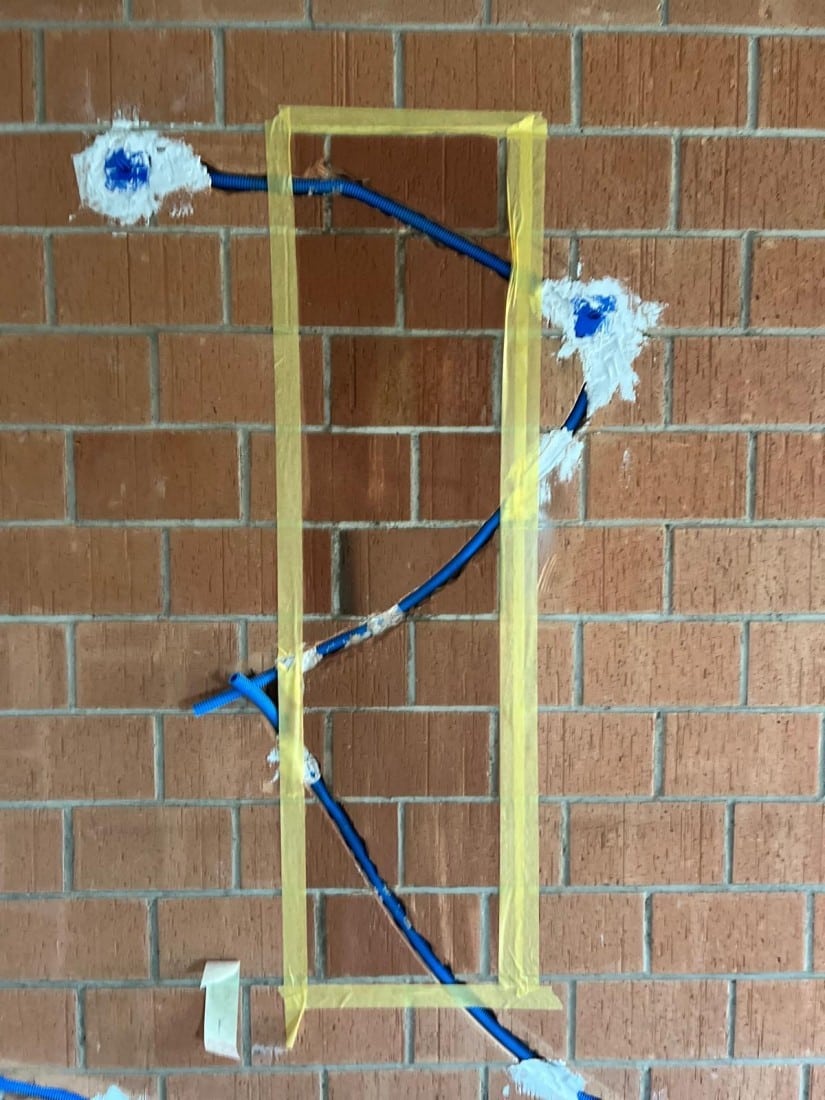 Installation von blauen Kabeln in einer Backsteinwand mit gelbem Klebeband markiert.