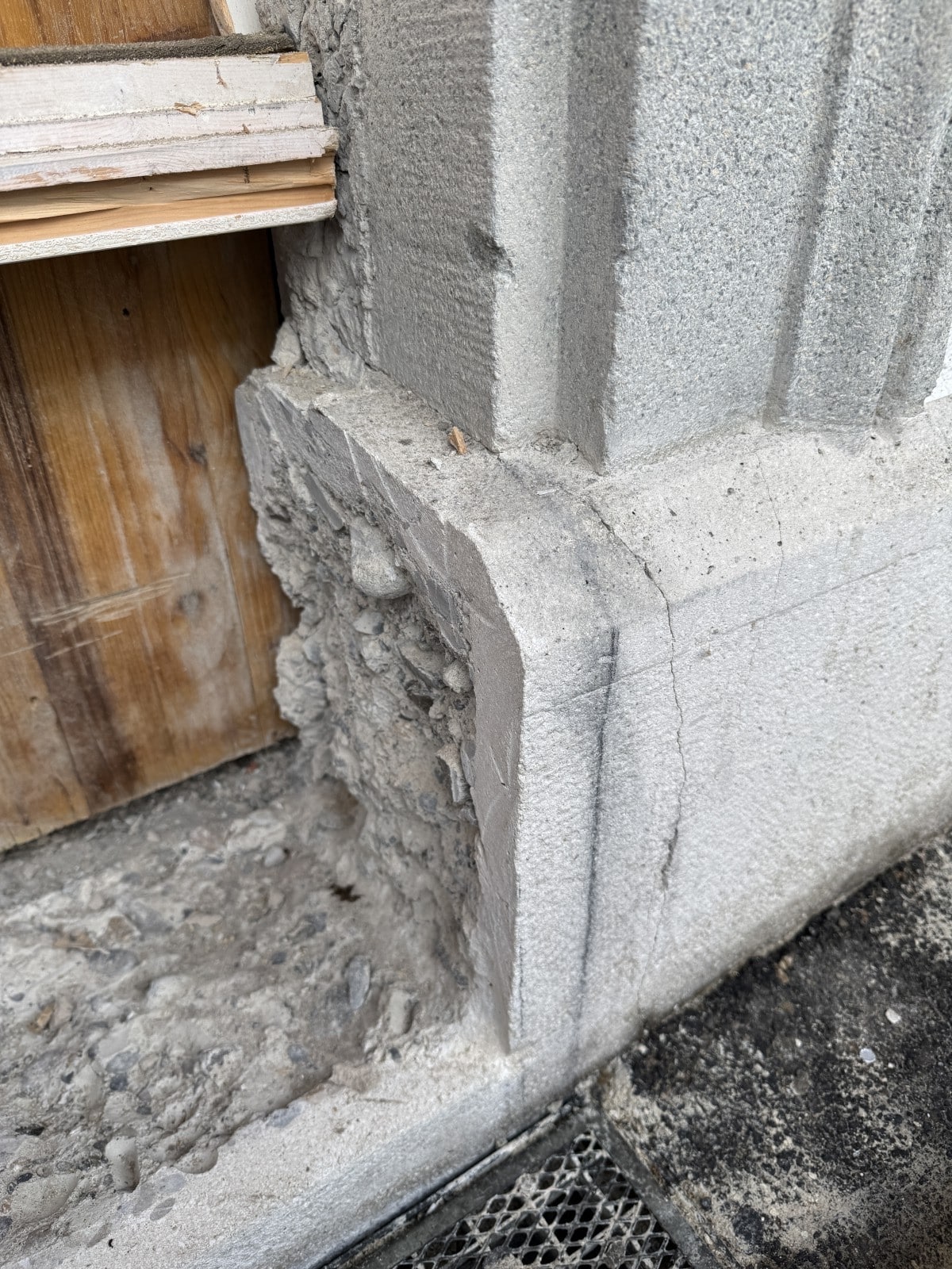 Nahaufnahme einer teilweise freigelegten Betonstruktur mit Rissen und Holzelementen, zeigt Bauschäden und Abnutzung.